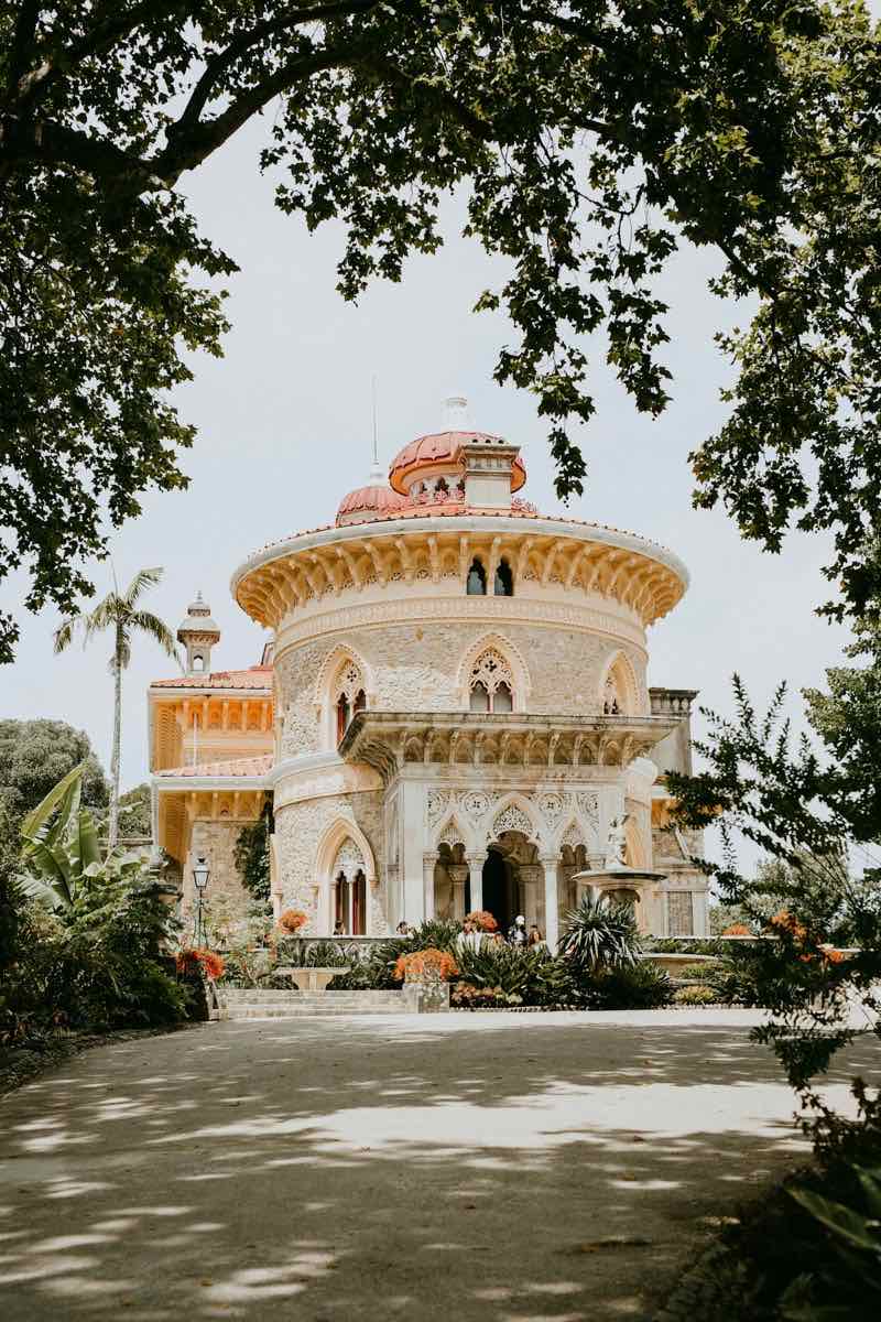 A rose-and-cream palace with a coral dome, framed by trees, palms and flowering plants